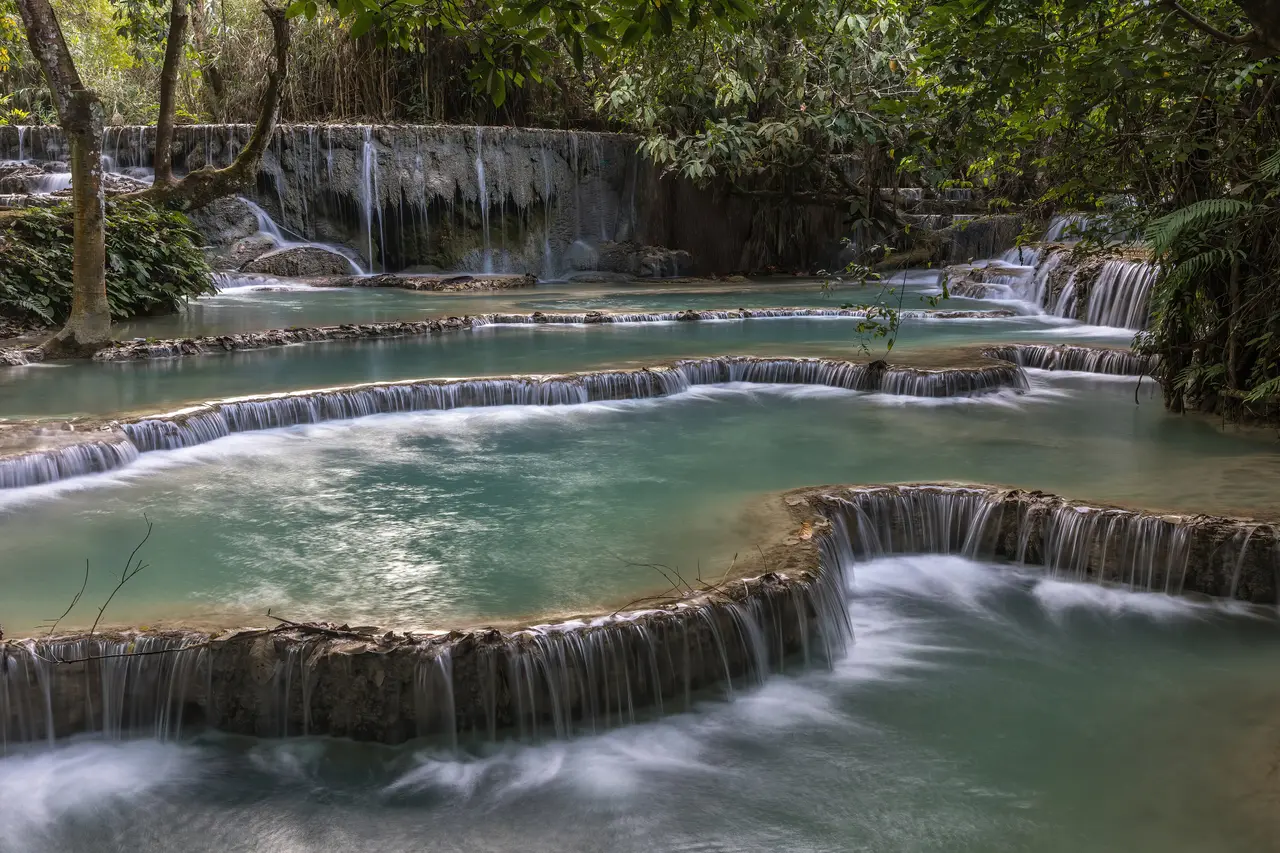 Water spilling over a series of limestone ledges into emerald pools at Kuang Si