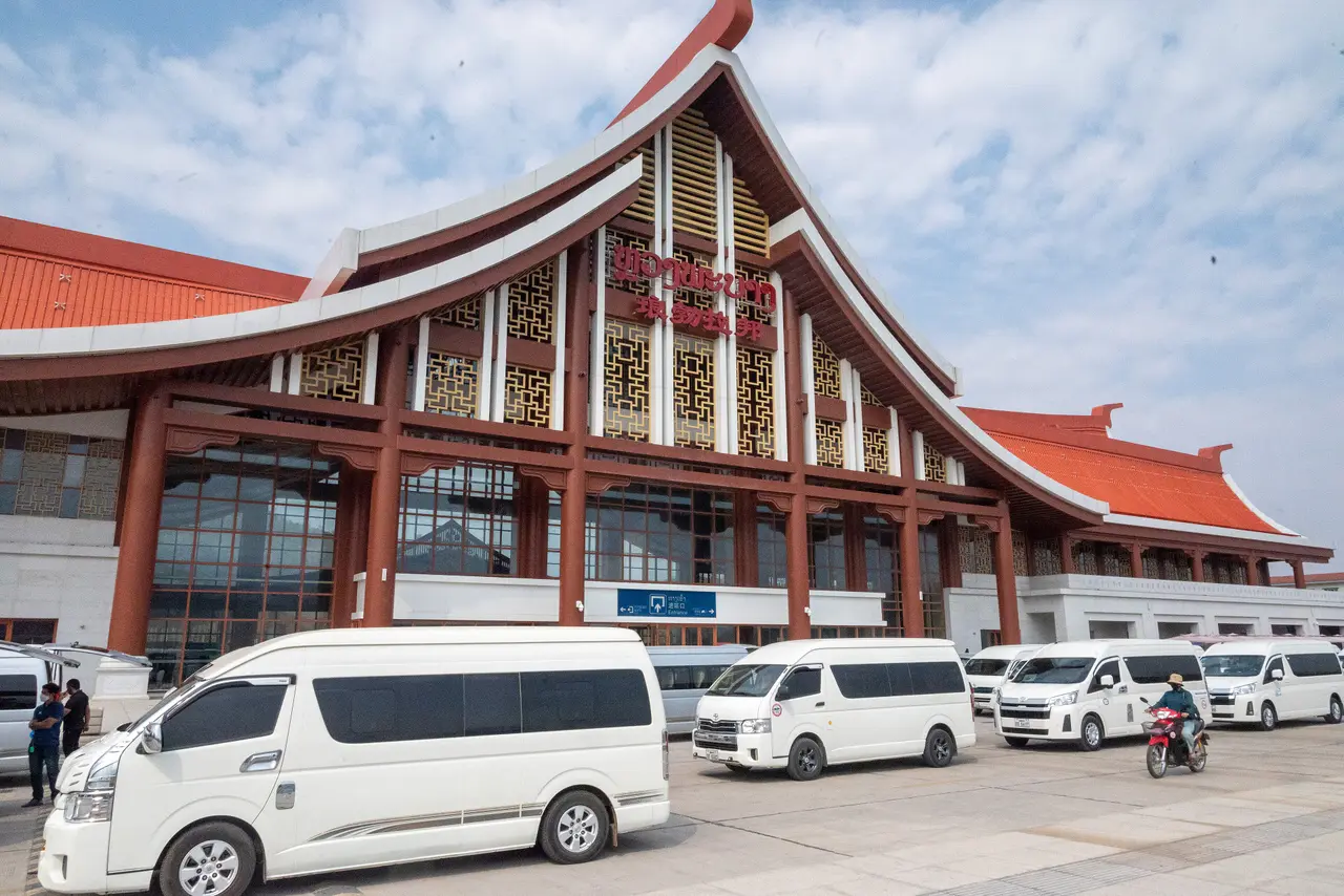 Minivans parked outside the large red-and-gold roofed Luang Prabang railway station