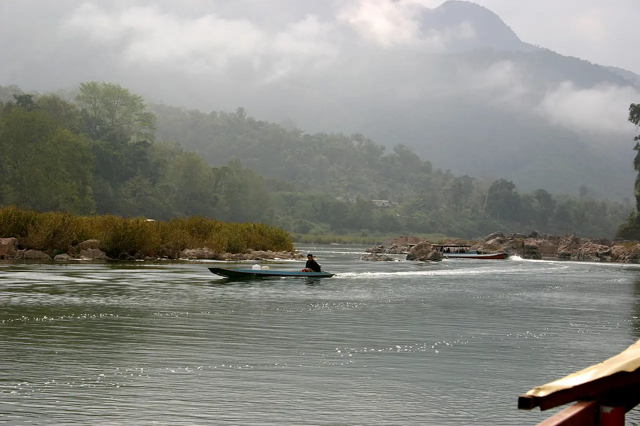 A small boat crossing the Nam Ou below misty forested hills