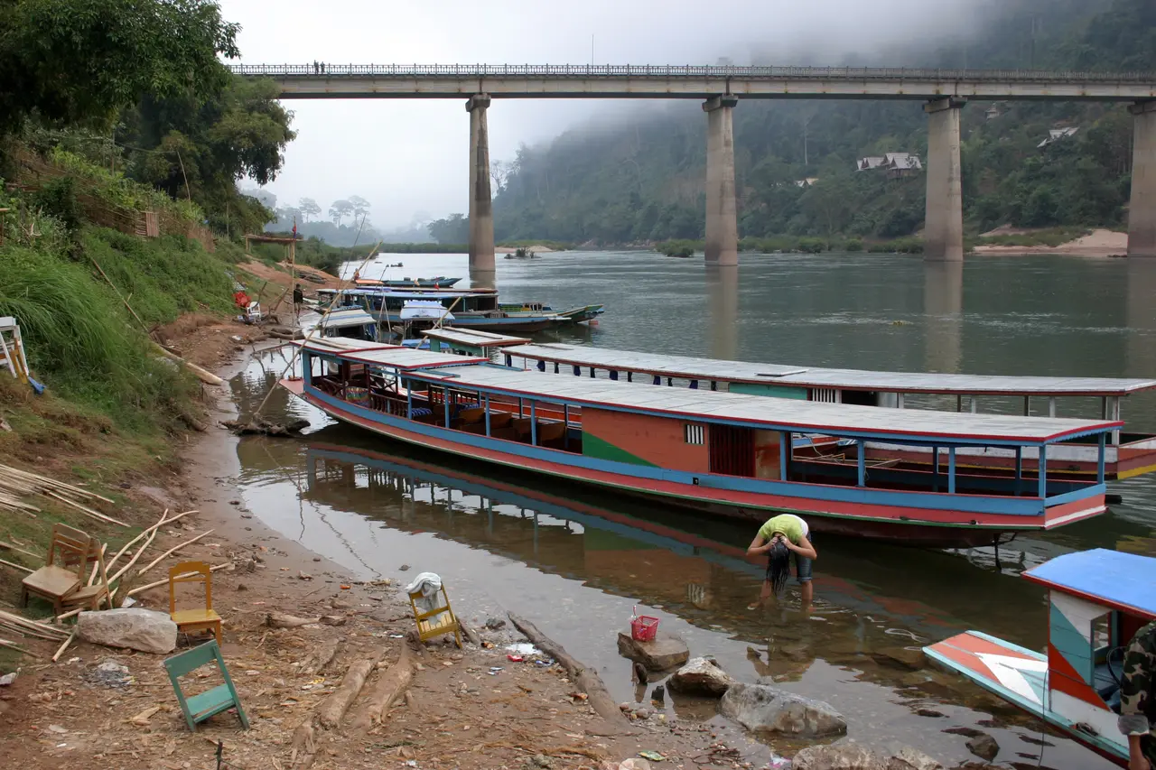 Long wooden passenger boats moored on the Nam Ou below the road bridge at Nong Khiaw