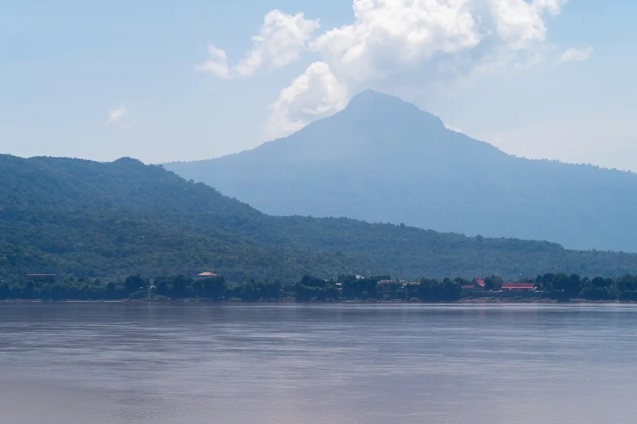 The Mekong at Pakse in daylight, with a pointed forested mountain rising beyond the river