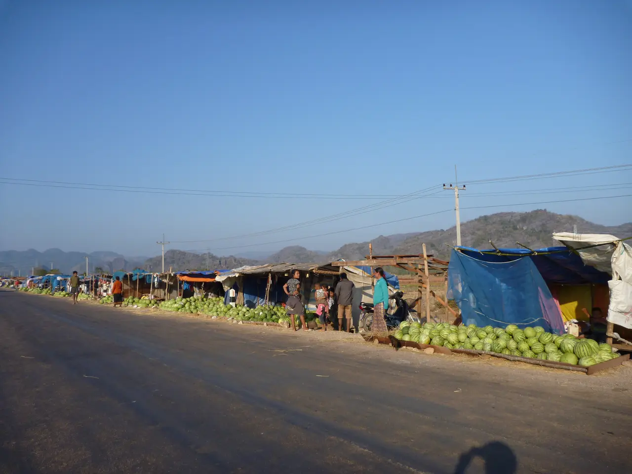 Roadside stalls selling watermelons on a paved road leading out of Thakhek towards hills